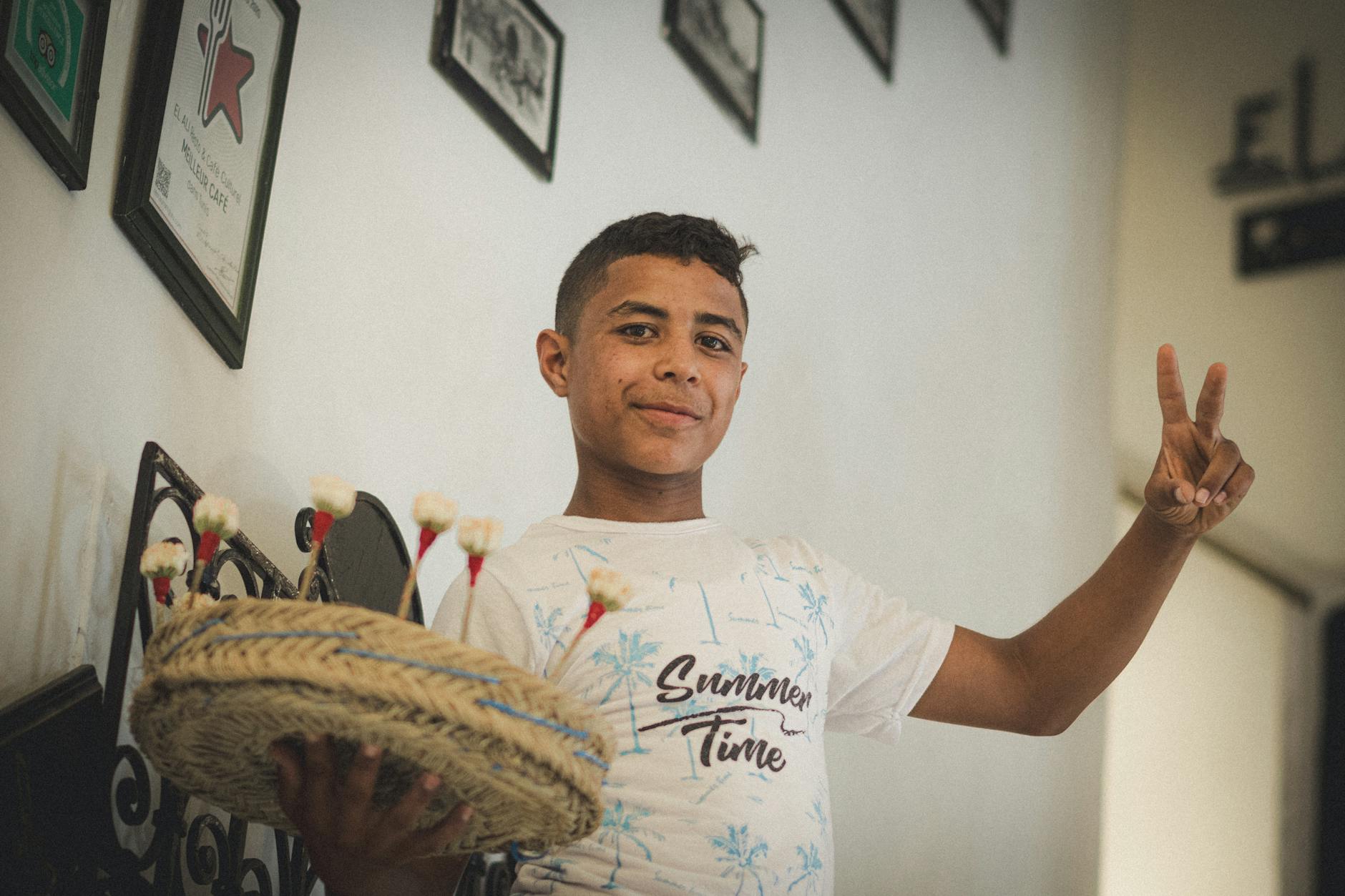 Uśmiechnięty tunezyjski chłopiec w pomieszczeniu pokazuje znak pokoju