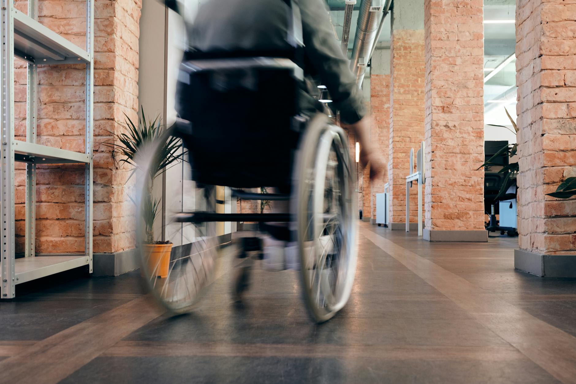 Osoba na wózku inwalidzkim szybko poruszająca się po korytarzu indoors