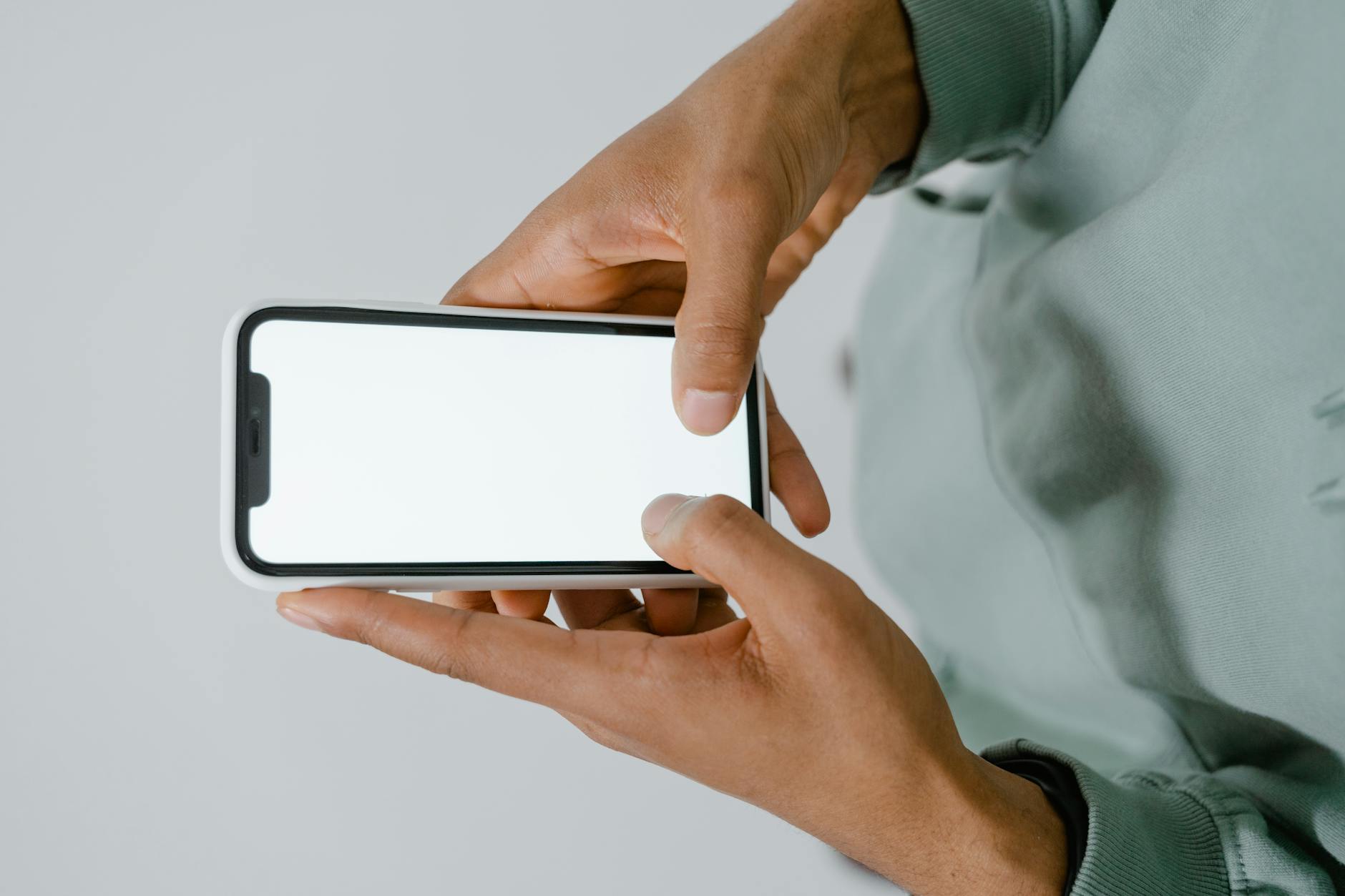 Dwie dłonie trzymają smartfon z pustym ekranem na jasnym tle