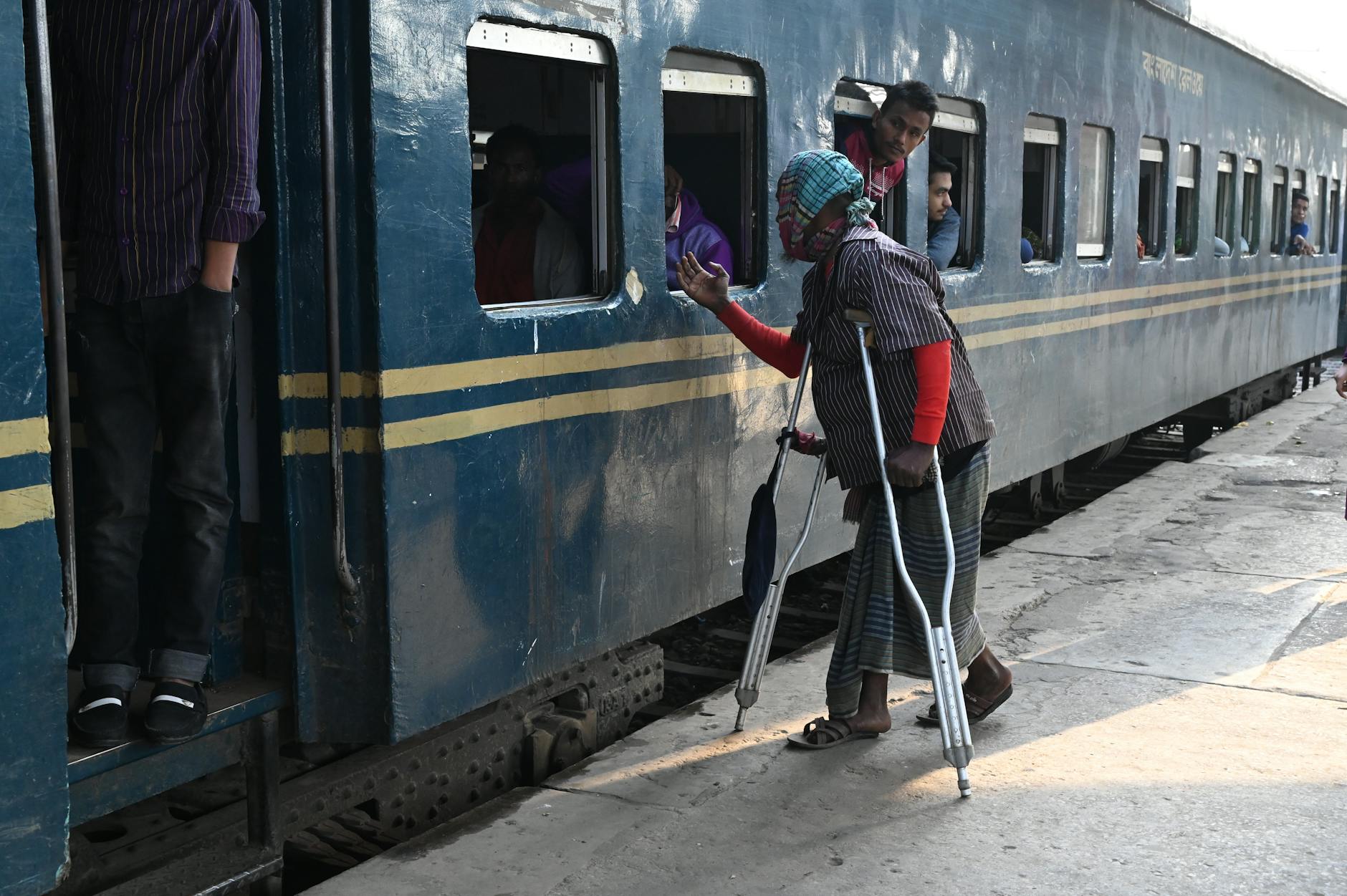 Starszy mężczyzna o kulach wsiada do pociągu z pomocą asysty