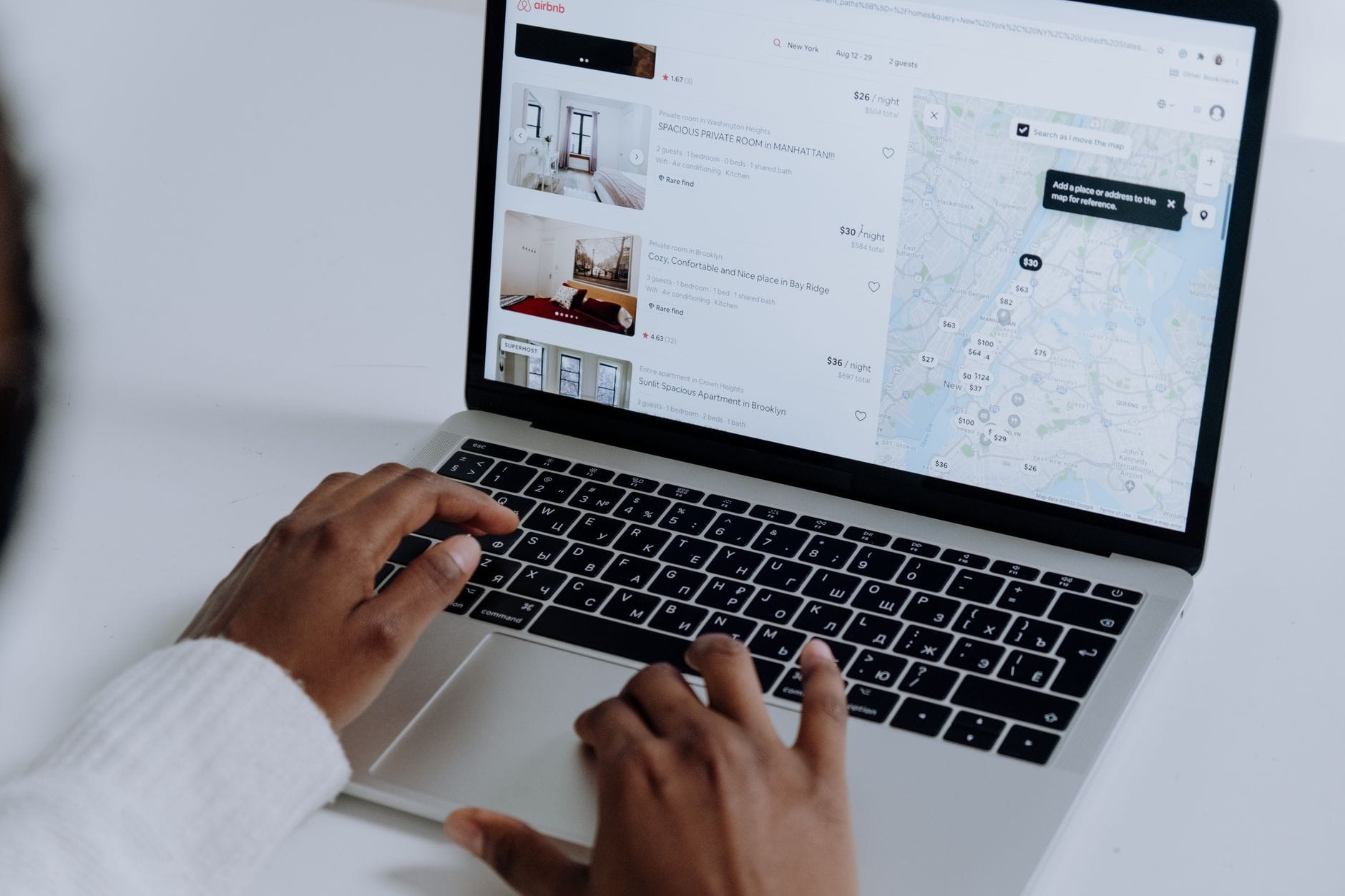 Dłonie na klawiaturze laptopa z wyszukiwarką noclegów i mapą