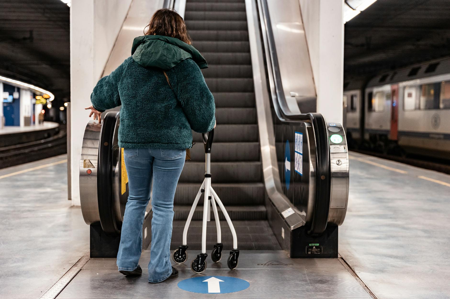 Kobieta z balkonikiem wjeżdża na ruchome schody na stacji metra