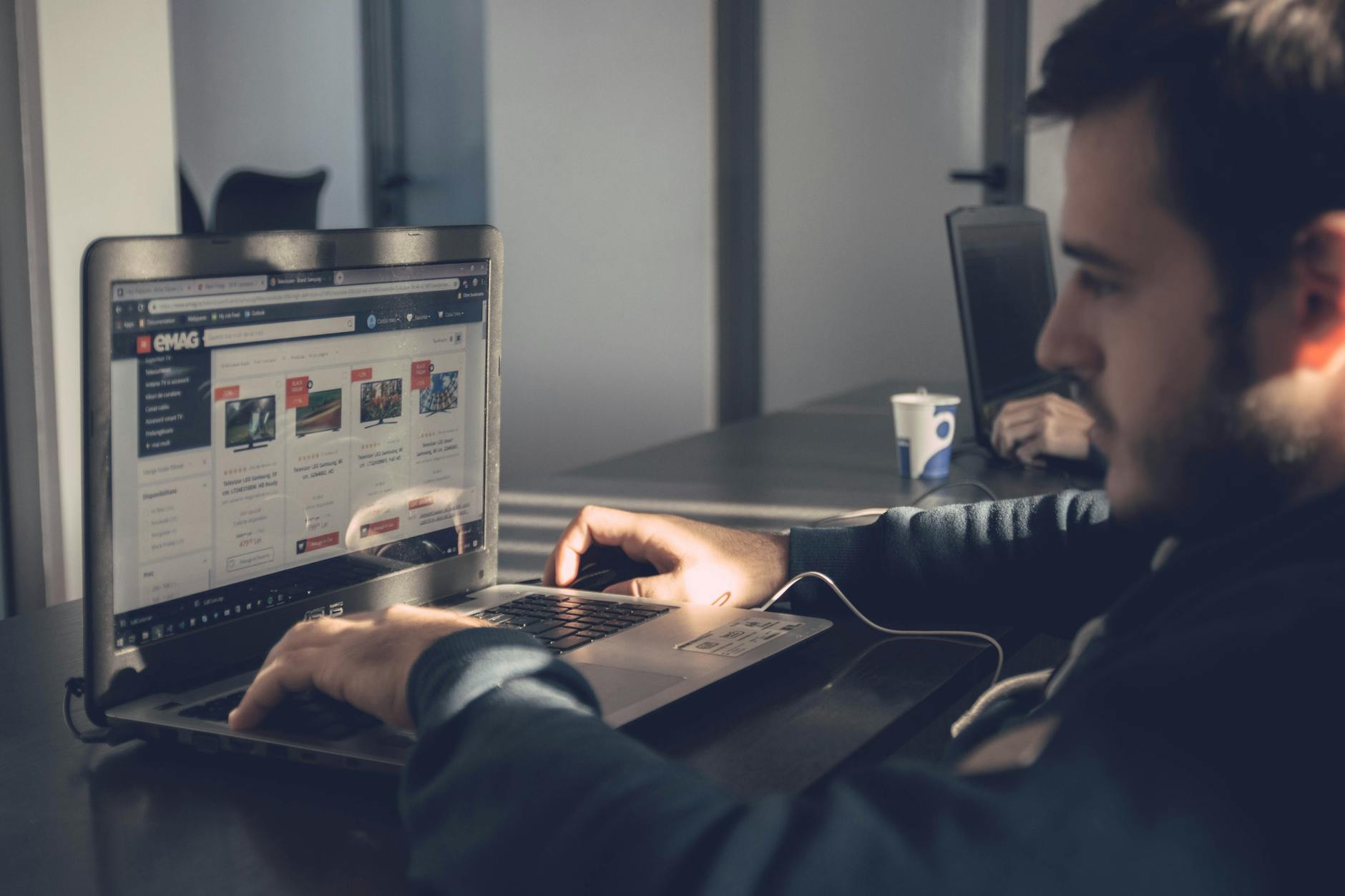 Mężczyzna w biurze przegląda na laptopie ofertę w sklepie internetowym