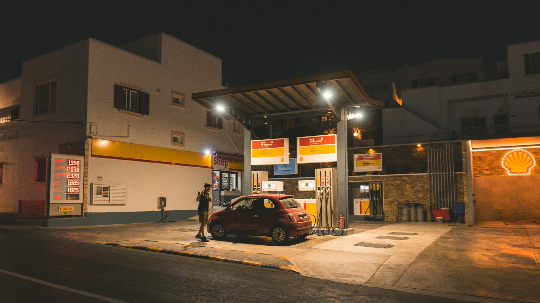 Osoba tankuje czerwone auto na oświetlonej stacji nocą