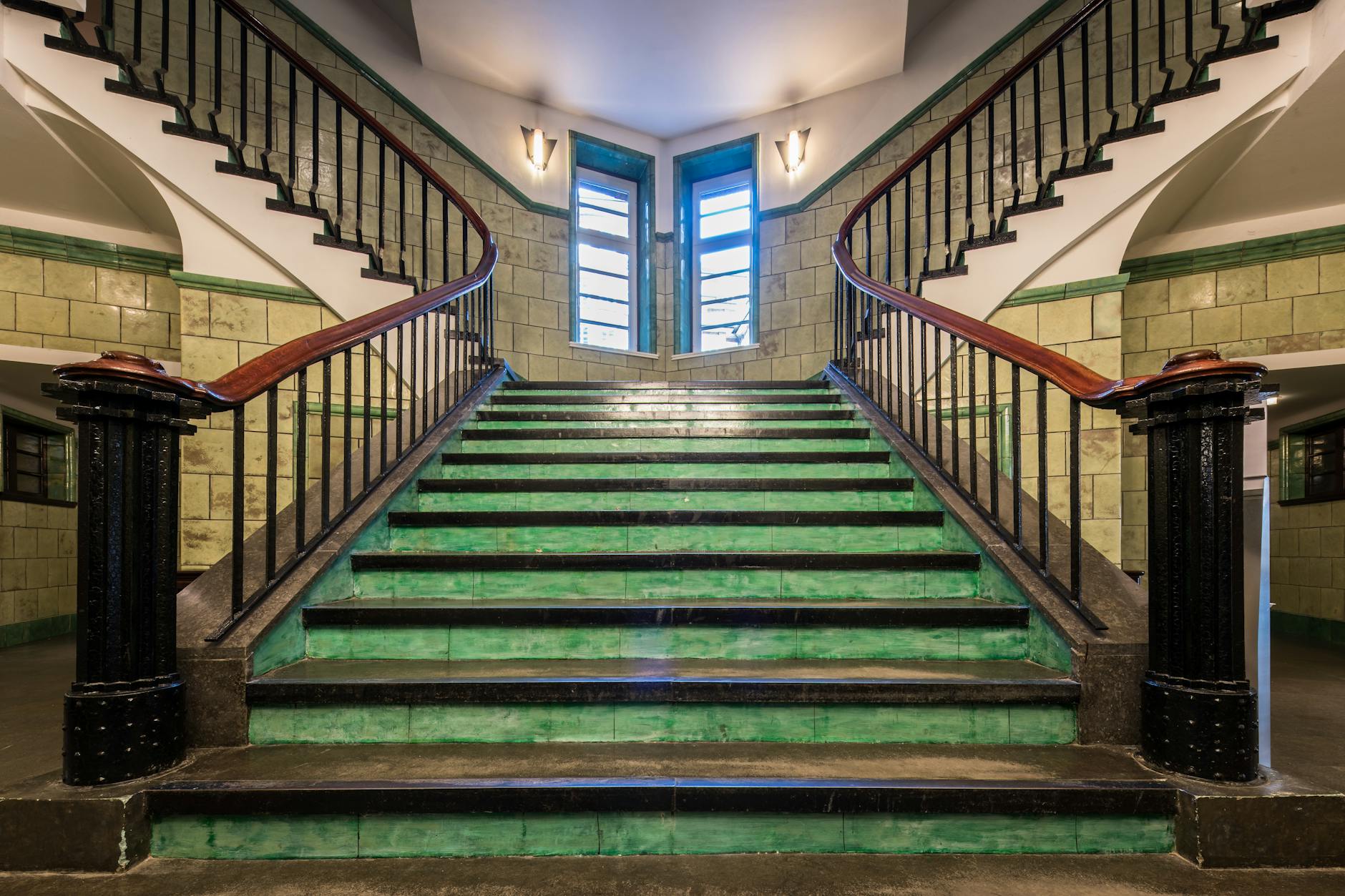 Zabytkowa klatka schodowa z zielonymi kafelkami i żelazną balustradą