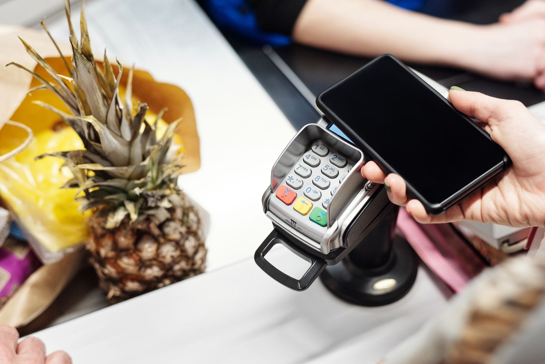 Płatność zbliżeniowa telefonem przy kasie, obok leży ananas