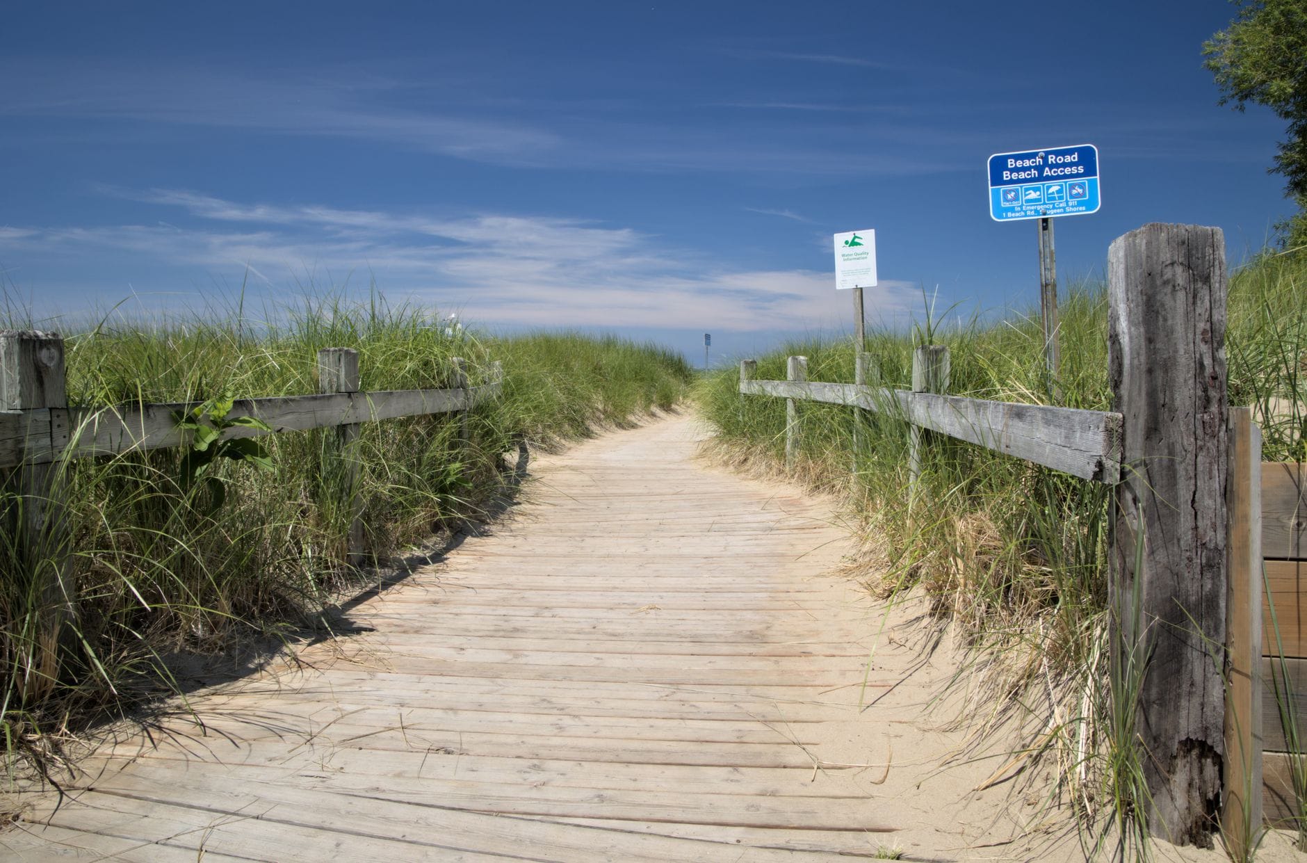 Drewniana ścieżka przez wydmy prowadzi na słoneczną, piaszczystą plażę