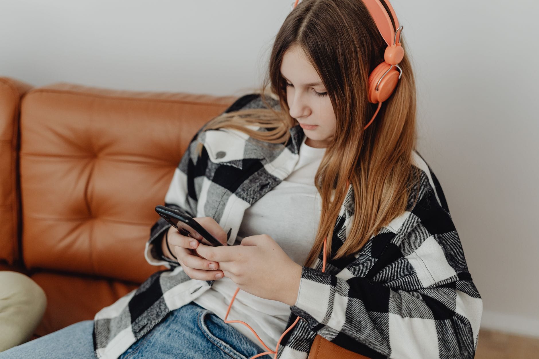 Nastolatka w słuchawkach słucha muzyki i korzysta ze smartfona na kanapie