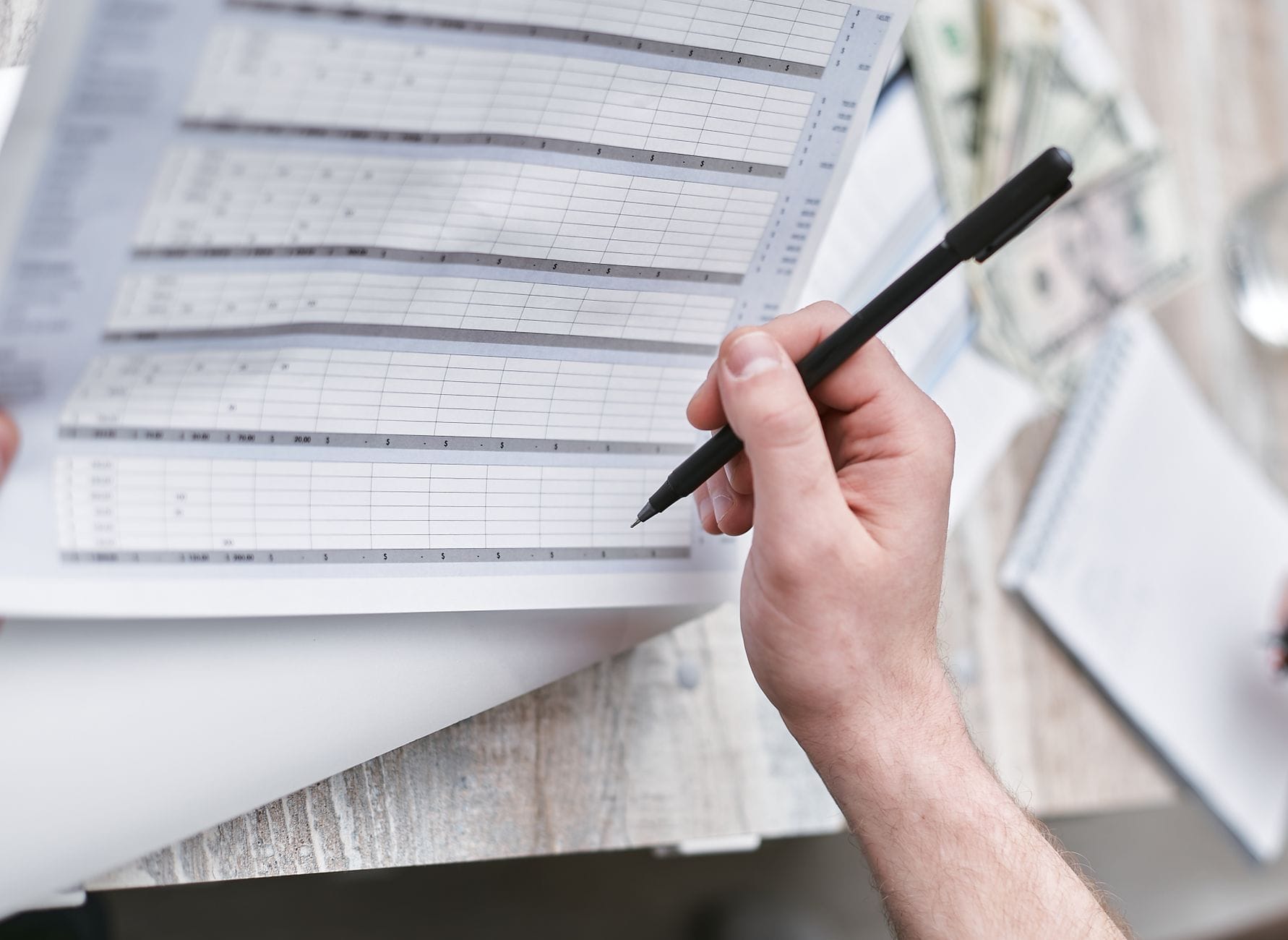 Osoba analizuje dokument finansowy z długopisem i gotówką obok