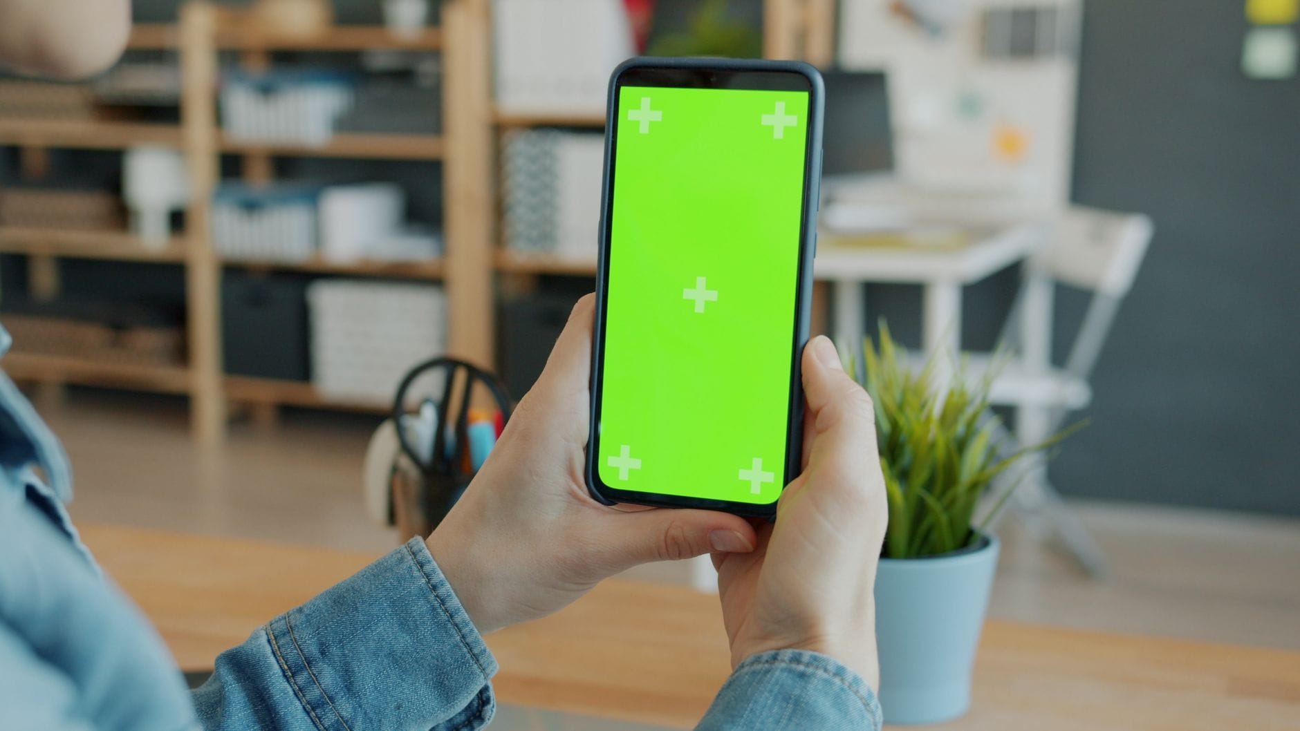 Osoba trzyma smartfon z zielonym ekranem w biurze