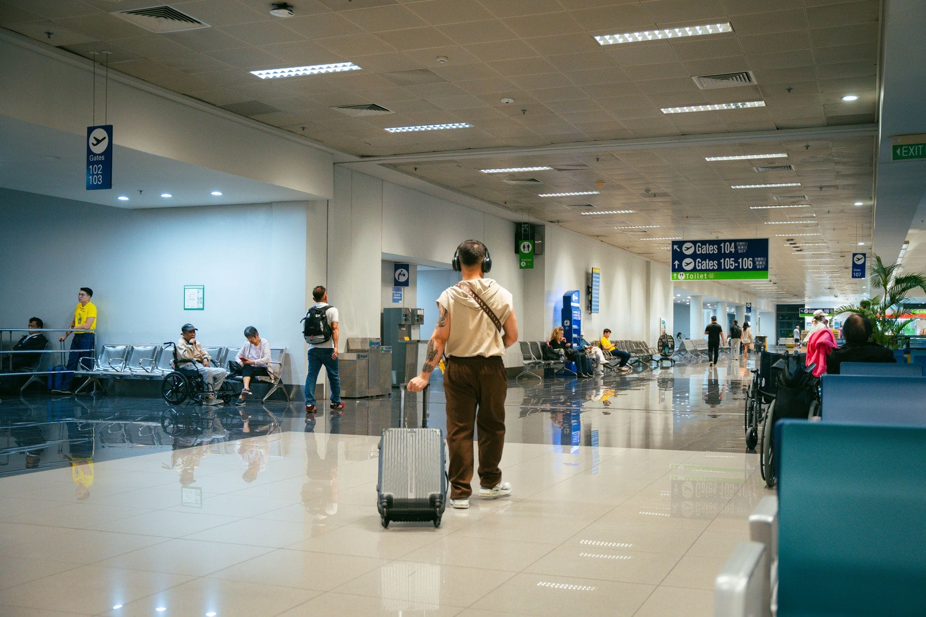 Pasażerowie w przestronnym terminalu lotniska, część siedzi, część idzie
